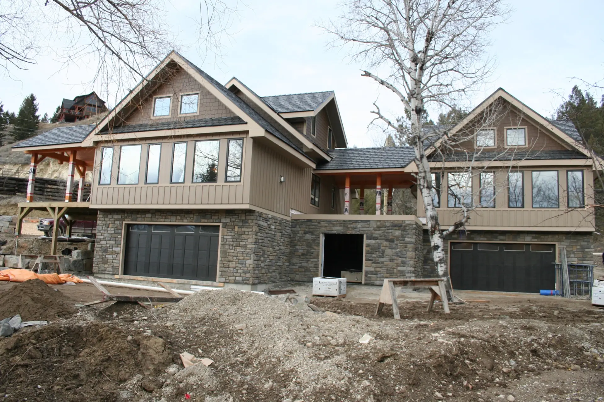 Custom home on a hillside lot with stone-clad walkout garages, board-and-batten upper storeys, covered timber decks and steep gabled roofs