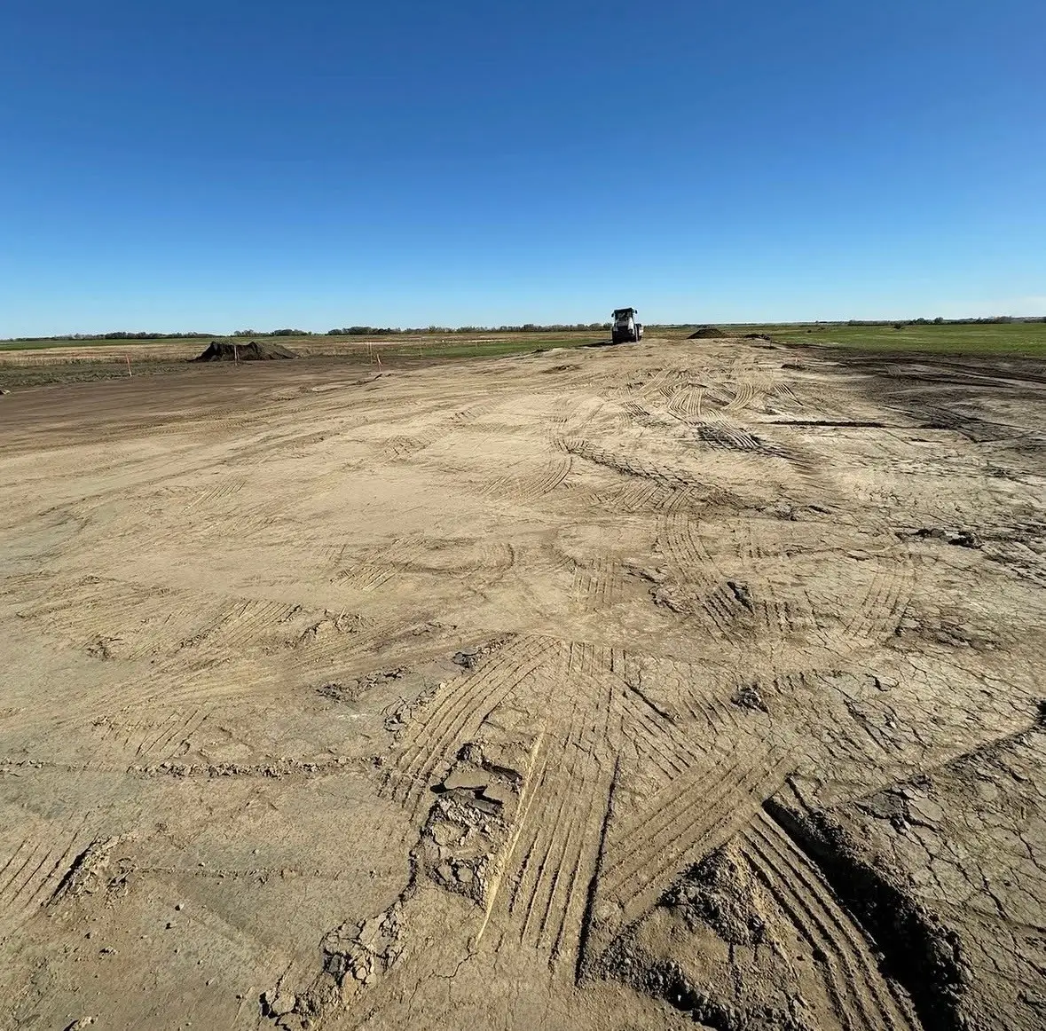 Graded and compacted building pad for the 35,224 square foot warehouse in Mountain View County, with survey stakes and a compactor