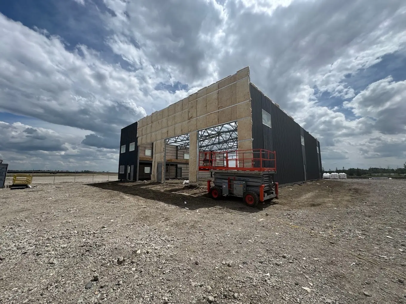 Steel building with dark metal cladding partially installed over exposed mineral wool insulation, with the overhead door opening framed out