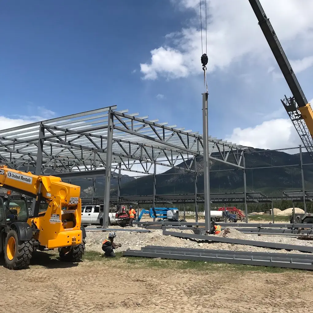Crane lifting a steel column into place during erection of a clear-span building frame in the Alberta foothills