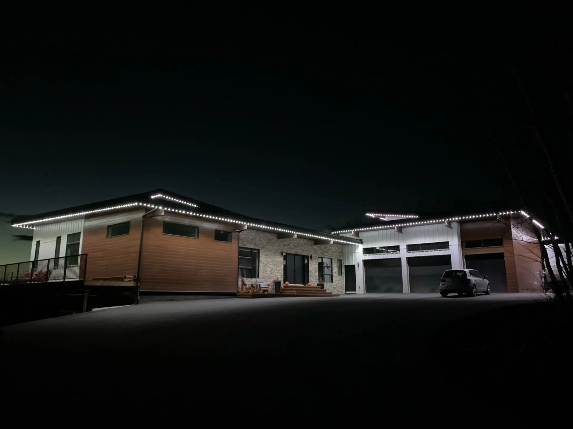 Front of the steel-frame residence at night, with a stone-clad entry, wood-tone and white cladding, and three garage doors