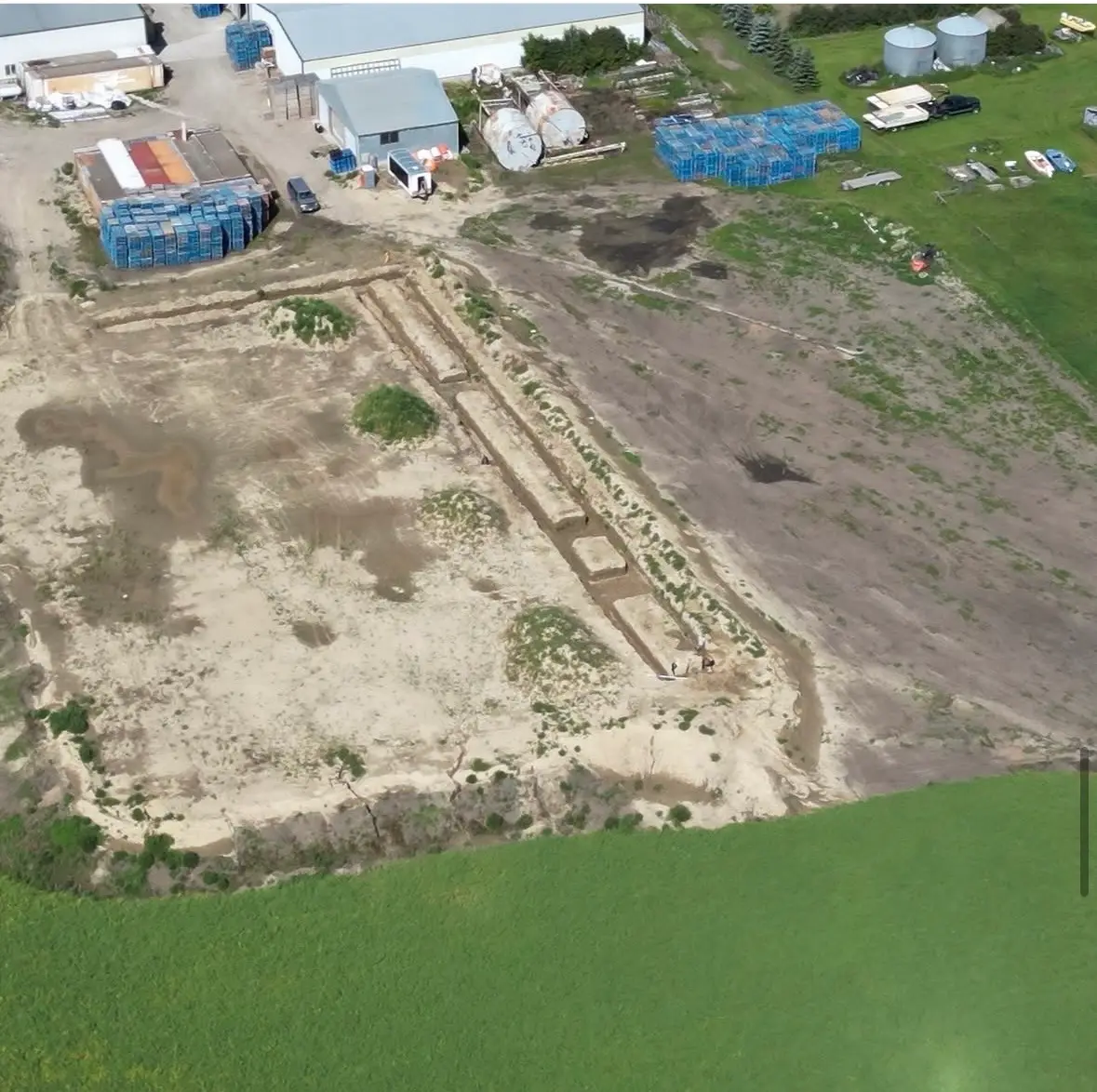 Aerial view of the Wheatland County site with the building footprint excavated and footings laid out, beside farm buildings and fields